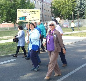 Zu sehen sind mehrere Mitglieder des BV Ueckermünde. Sie laufen auf der Straße und halten ein Vereinsschild hoch mit der Aufschrift "Für Selbstbestimmung und Würde"