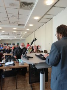 Das Bild zeigt den Referenten Hammerschmidt während seiner Rede, sowie die Mitgliederversammlung.