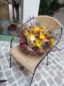 Das Bild zeigt einen Rattanstuhl, auf welchem ein buntes Blumengesteck steht. 